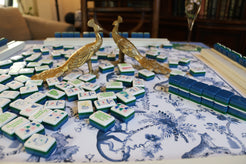 Mahjong game with decorative tiles and peacock figurines on a patterned tablecloth.