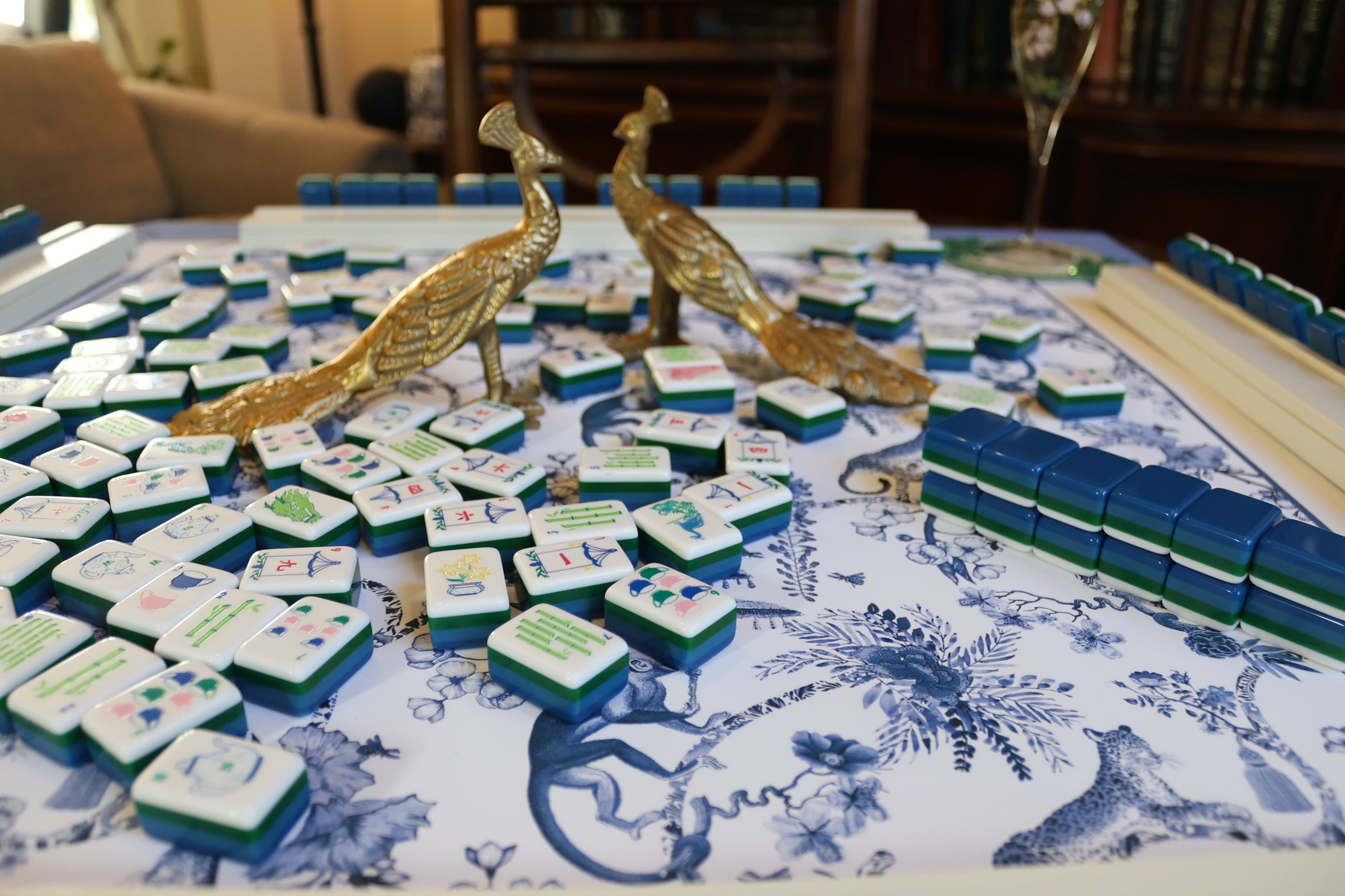 Mahjong game with decorative tiles and peacock figurines on a patterned tablecloth.